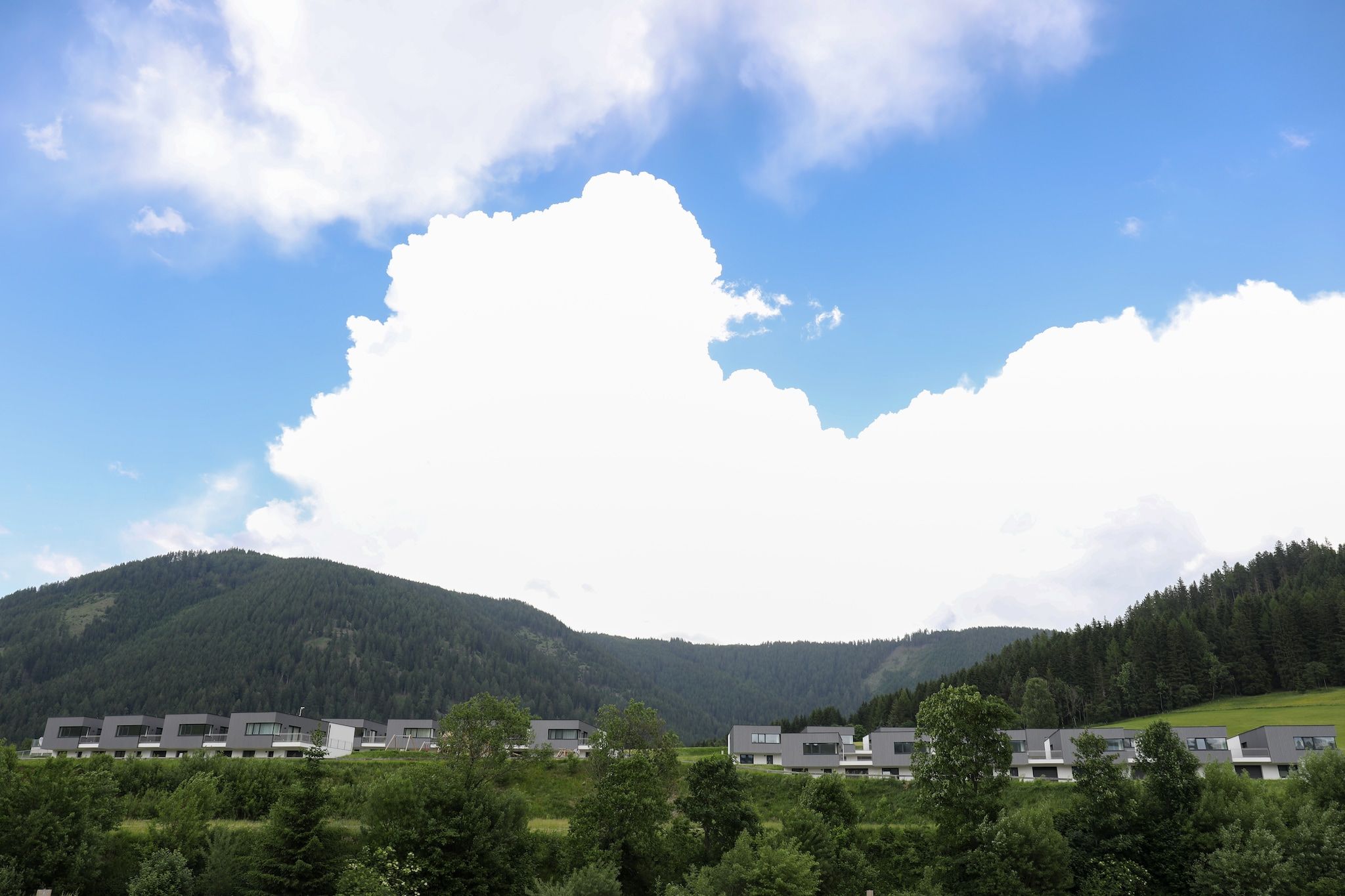 Un complejo moderno de varias unidades, con colinas verdes y un cielo despejado al fondo.