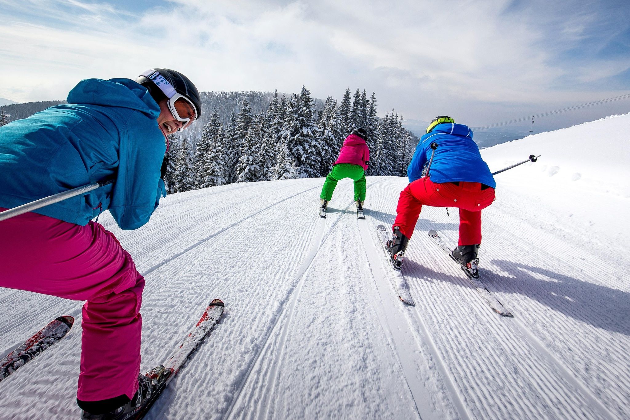 Trois skieurs sur une pente enneigée, avec des arbres en arrière-plan.
