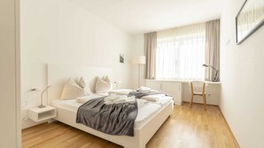 A modern bedroom with a bed, bedside table, lamp, and a desk with a chair.