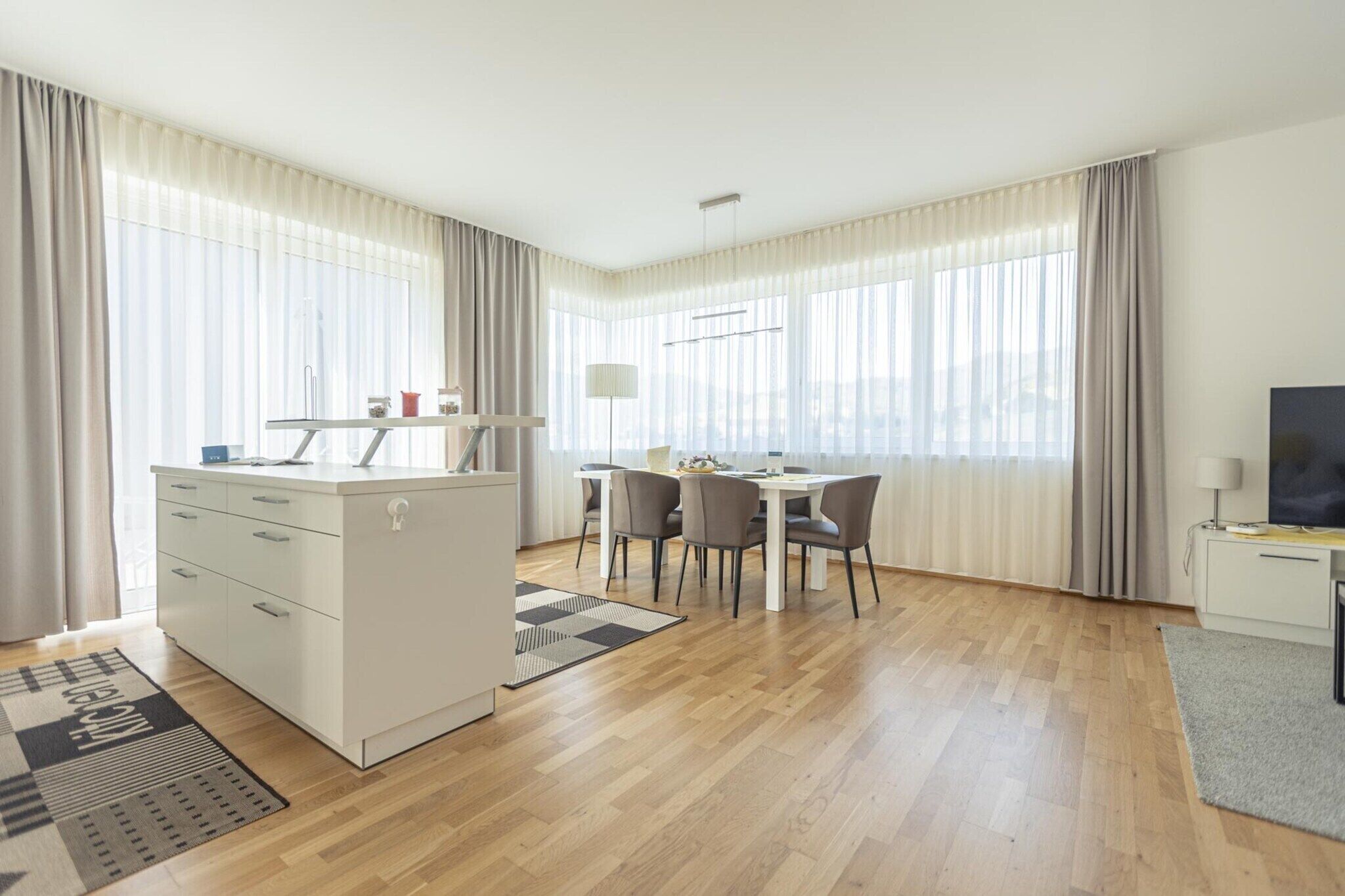 Ein modernes Hotelzimmer mit einer Küchenzeile, einem Essbereich und einem großen Fenster mit Vorhängen.
