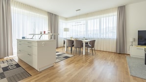 A modern hotel room with a kitchenette, a dining area, and a large window with curtains.