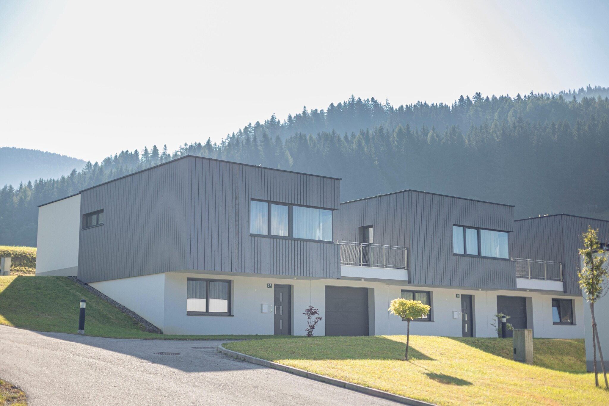 A modern two-story residential building with a flat roof, large windows, and a small balcony.