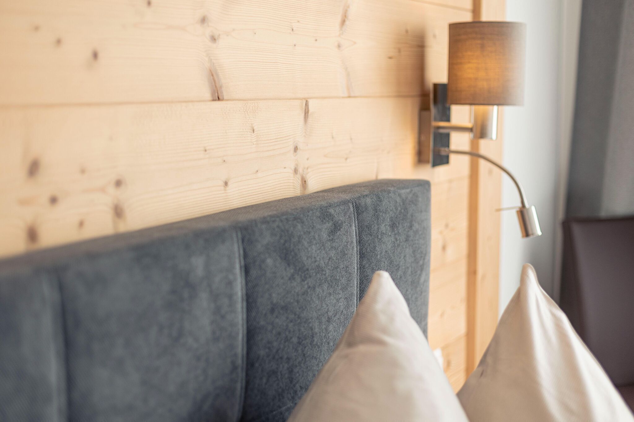 Eine Ecke eines Zimmers mit einer Holzwand, einem grauen Sofa und einer Wandlampe.