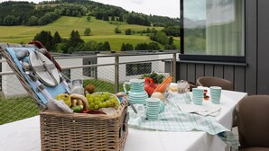 Ein Picknicktisch mit Korb, Tellern, Tassen und Blick auf eine grüne Landschaft.
