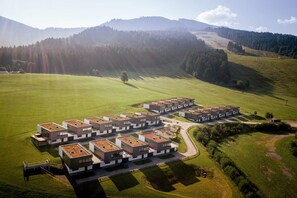An aerial view of a modern residential complex with multiple buildings, green lawns, and a hilly landscape in the background.