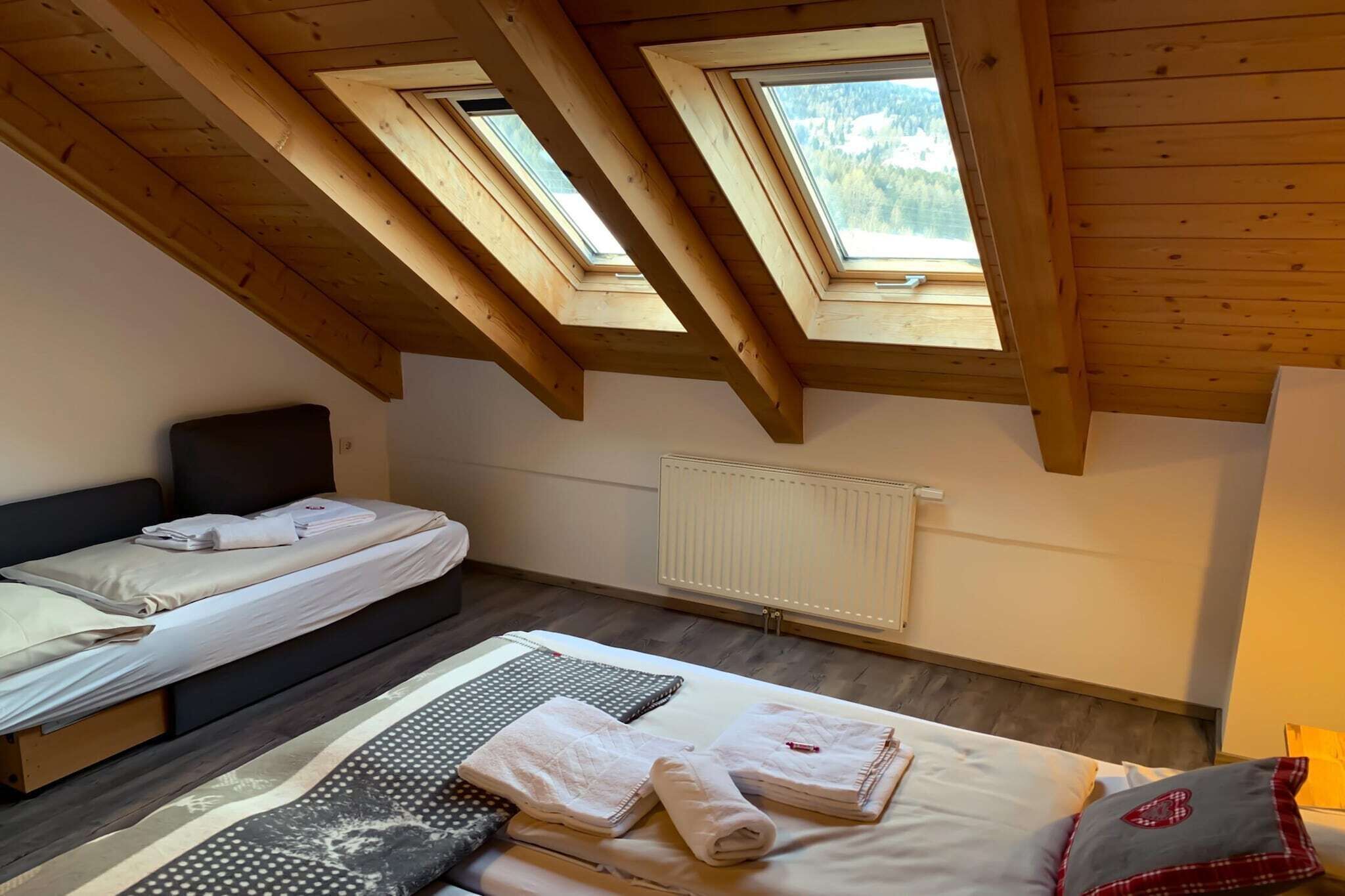 Quarto com duas camas, claraboias, radiador e janela com vista para árvores.