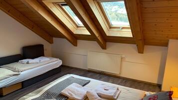 Quarto com duas camas, claraboias, radiador e janela com vista para árvores.