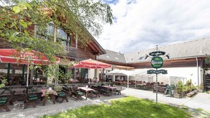 Un área de café al aire libre con mesas y sillas de madera, sombrillas rojas y un letrero que dice 'Güssler'.