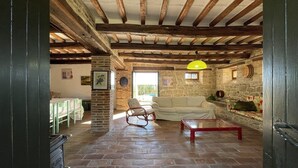 Uma sala de estar rústica com vigas de madeira aparentes, lareira de pedra, sofá branco e mesa de centro vermelha.