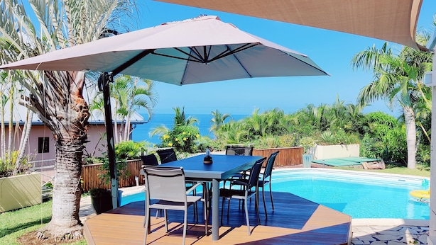 Eine Terrasse im Freien mit Tisch und Stühlen, einem Pool und Blick auf den Ozean.