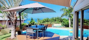 An outdoor patio with a table and chairs, a pool, and a view of the ocean. - Big Blue Villa (Saint Paul)