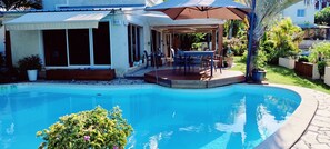 A swimming pool with a covered patio area, a table and chairs, and potted plants. - Big Blue Villa (Saint Paul)