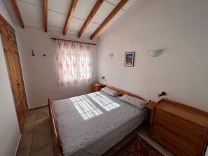 A bedroom with a bed, wooden headboard, bedside tables, a wardrobe, and a window with curtains.