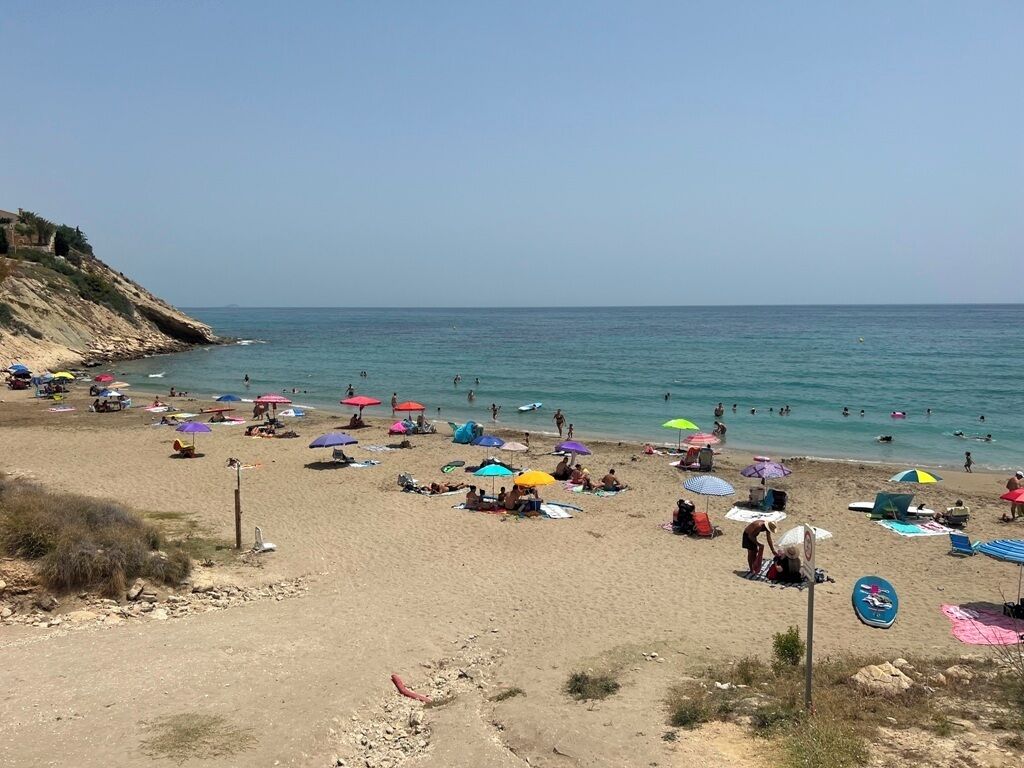 A beach with people sunbathing and swimming, colorful umbrellas, and a clear sky.