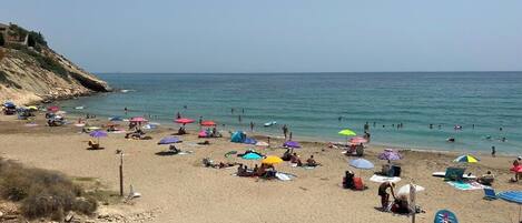 A beach with people sunbathing and swimming, colorful umbrellas, and a clear sky.