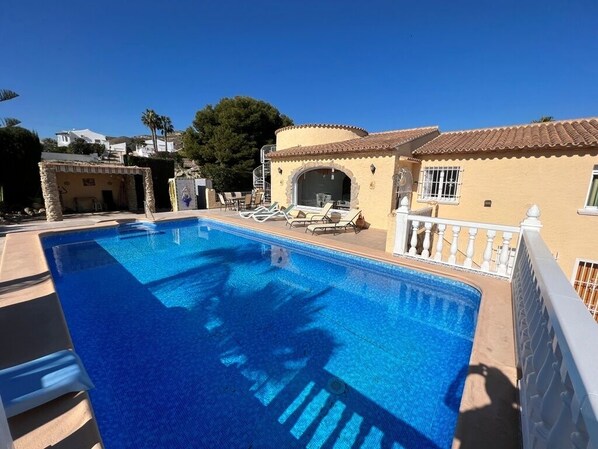 A swimming pool with lounge chairs, a stone structure, and a building with a tiled roof. - Villa with private pool, large garden and incredible sea view! (El Campello)