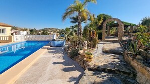 Una piscina con un sendero de piedra, palmeras y un arco de piedra.
