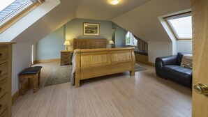 A bedroom with a sloped ceiling, a wooden bed, a nightstand, a dresser, a bench, a sofa, and a skylight. - Exceptionally spacious 5 star holiday home with 4 bedrooms, large living room, dining kitchen, log f (Aberfeldy)