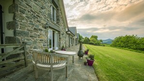 A stone building with a wooden bench and table outside, surrounded by a well-maintained lawn and a scenic view of hills. - Exceptionally spacious 5 star holiday home with 4 bedrooms, large living room, dining kitchen, log f (Aberfeldy)