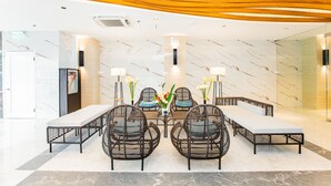 Um lobby moderno com parede de mármore, área de estar central com cadeiras de vime e um banco, e teto decorativo.