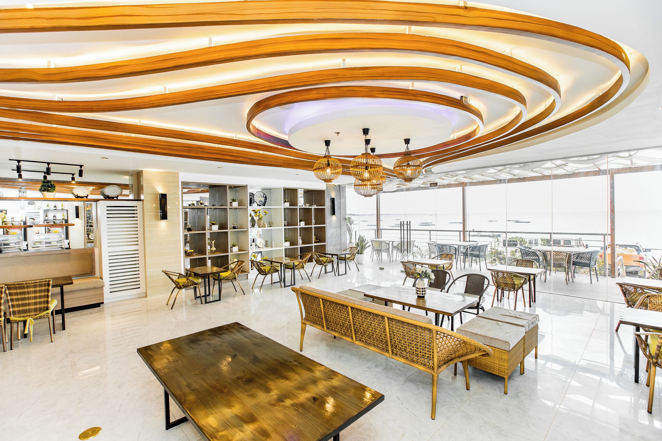 A modern interior with a high ceiling, circular wooden patterns, and a dining area with wicker furniture.