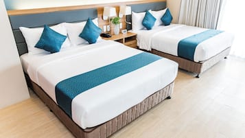 A hotel room with two beds, each with white bedding and blue accents, a nightstand with a lamp and a phone, and a wooden headboard.