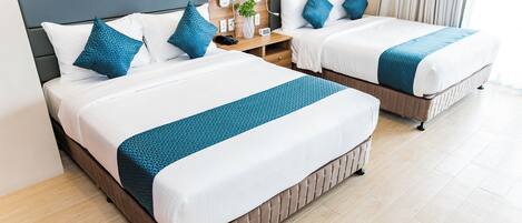 A hotel room with two beds, each with white bedding and blue accents, a nightstand with a lamp and a phone, and a wooden headboard.