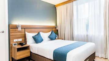 A hotel room with a bed, bedside table, lamp, and curtains.
