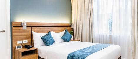 A hotel room with a bed, bedside table, lamp, and curtains.