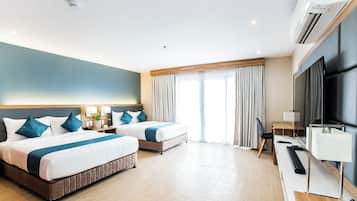 A hotel room with two beds, a desk, a TV, and an air conditioning unit.