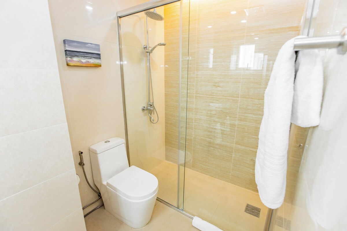 A modern bathroom with a glass-enclosed shower, a toilet, and a towel rack.