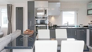 Une cuisine moderne dotée d’un îlot central, d’appareils électroménagers intégrés et d’un coin repas avec une table à plateau en verre et des chaises blanches.