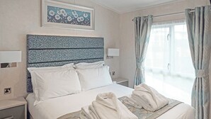 Une chambre d’hôtel comprenant un lit, une tête de lit, une table de chevet, une fenêtre avec des rideaux et un tableau encadré au mur.
