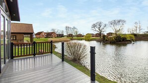 A wooden deck with a railing overlooking a calm lake, surrounded by residential buildings and bare trees. - 1 bedroom accommodation in Swinethorpe, Nr Lincoln (Swinethorpe, Nr Lincoln)
