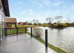 Una terraza de madera con barandilla que da a un lago tranquilo, rodeada de edificios residenciales y árboles sin hojas.