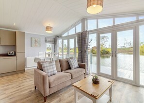 A modern living room with a sofa, a coffee table, and large windows overlooking a body of water. - 2 bedroom accommodation in Swinethorpe, Nr Lincoln (Swinethorpe, Nr Lincoln)