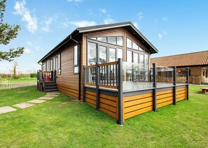 Una cabaña moderna de madera con ventanas amplias, una terraza y una escalera que lleva a la entrada.