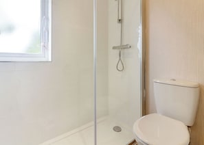 Un baño con ducha de vidrio, inodoro y ventana.