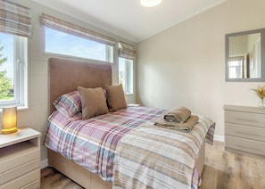 A bedroom with a bed, bedside table, dresser, and a window with curtains.