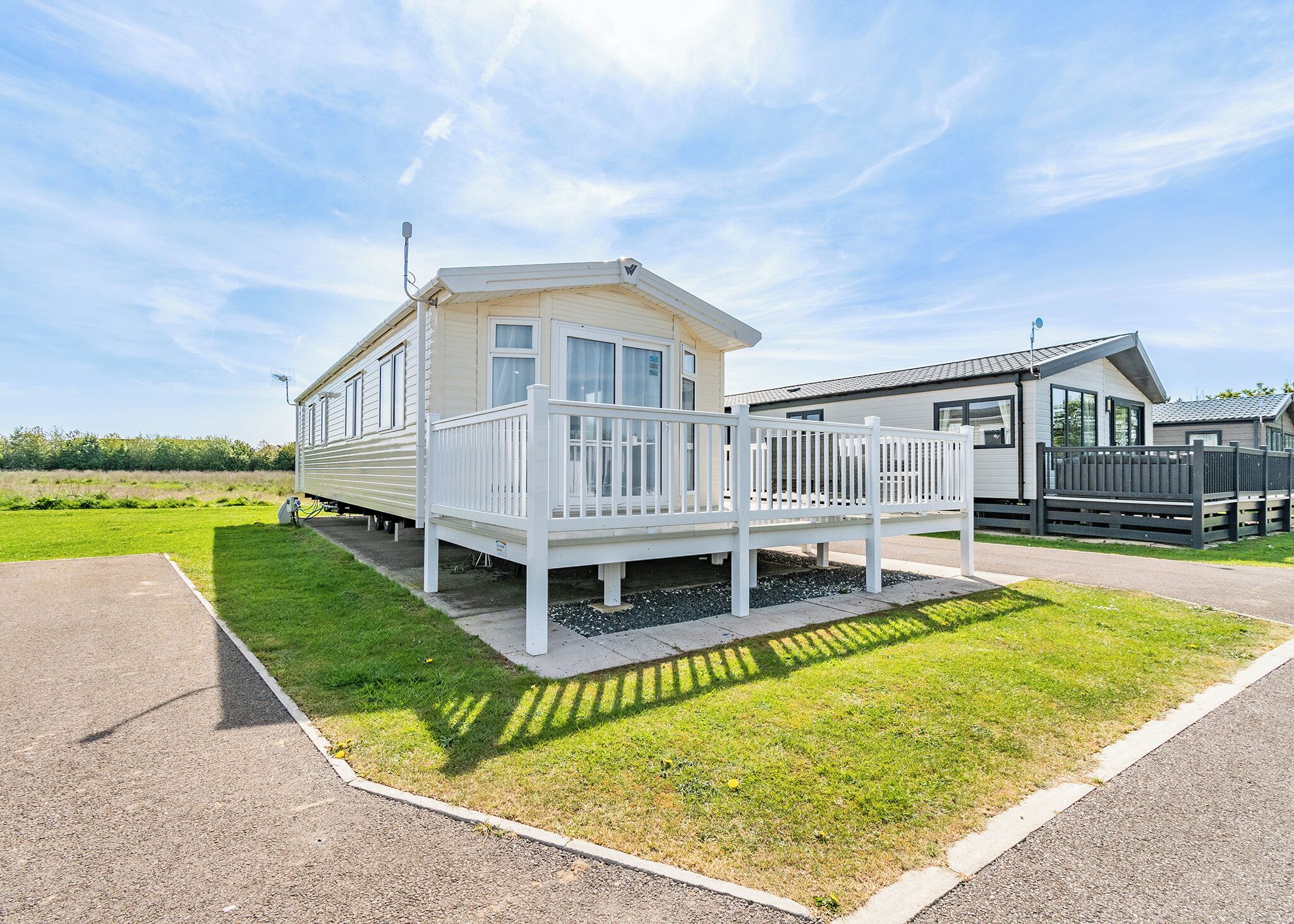 A mobile home with a deck, a fenced yard, and a clear sky.
