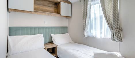 Un dormitorio con dos camas, cabeceros de madera, mesitas de noche pequeñas y una ventana con cortinas.