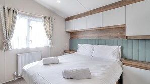 Un dormitorio con cama, cortinas blancas, cabecero de madera y un radiador.
