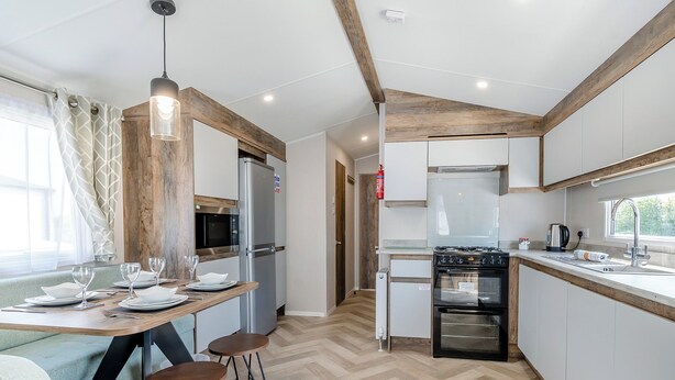 Una cocina moderna con techo de madera, electrodomésticos de acero inoxidable, un comedor con mesa dispuesta para cuatro comensales y un piso con estampado tipo espiga.