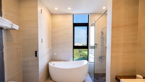 A modern bathroom with a freestanding bathtub, a glass shower enclosure, and a view of greenery outside.