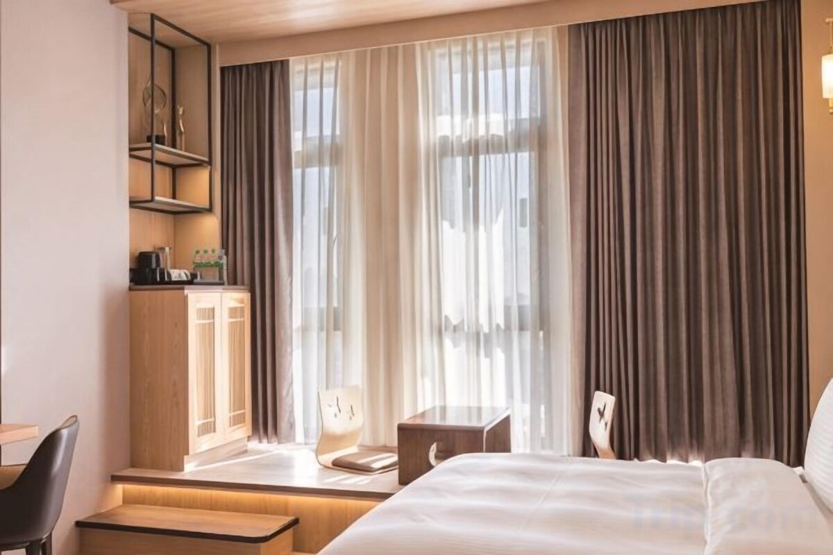 A hotel room with a bed, a desk, a chair, and a window with curtains.