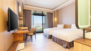 A hotel room with a large flat-screen TV, a desk with a chair, two beds, and a balcony with curtains.