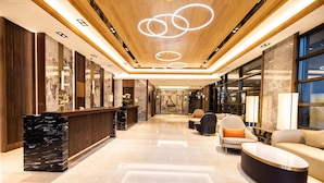 A modern lobby with a marble reception desk, seating area, and a ceiling with circular light fixtures.