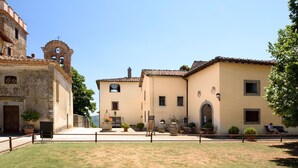 A courtyard with a building featuring a bell tower, a small archway, and a seating area with tables and chairs.