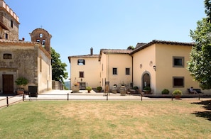 A courtyard with a building featuring a bell tower, a small archway, and a seating area with tables and chairs.