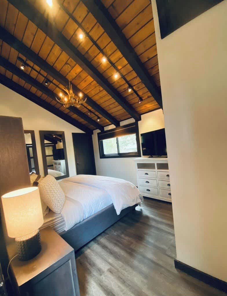 A bedroom with a wooden ceiling, a bed, a dresser, and a nightstand.